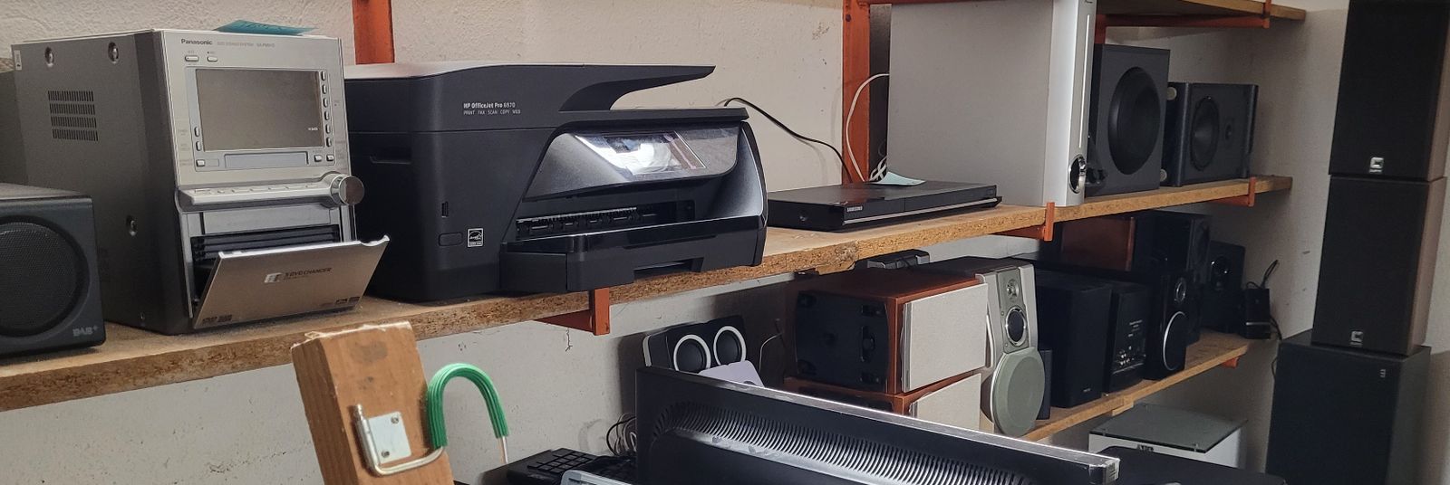 Regal mit gebrauchten Geräten: Stereoanlage, Drucker, Blu-ray-Player und mehrere Lautsprecher